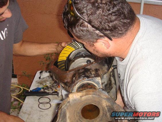 Two guys looking at a differential gear assembly with yellow and black teeth