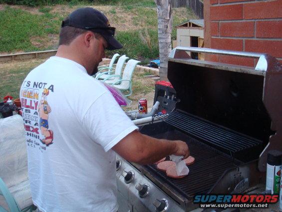 Guy in a cap and t-shirt grilling burgers on a gas grill in a backyard
