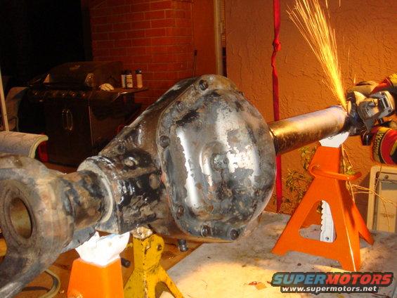 Rear axle assembly on jack stands, being worked on with an angle grinder. Sparks are flying