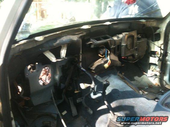 Interior of a dismantled vehicle, showing exposed wires, dashboard components, and pedals