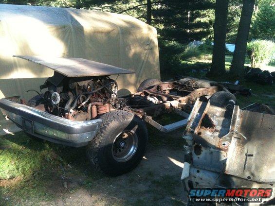 Disassembled truck chassis with engine exposed, hood up, in a yard