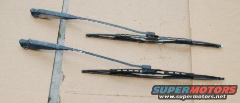 Two black windshield wiper arms and blades on a light brown surface