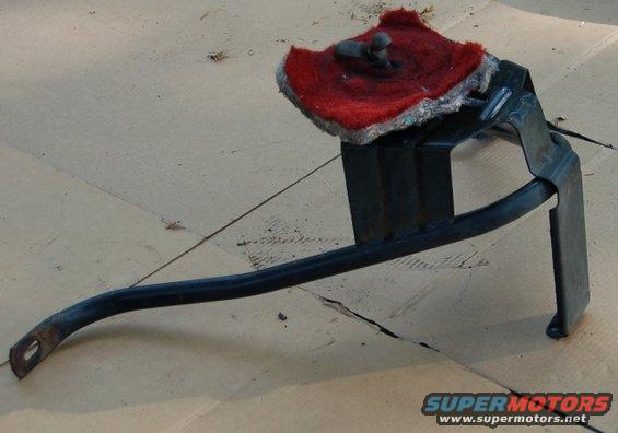 Black metal automotive part with a red buffing pad attached to a bracket, resting on cardboard