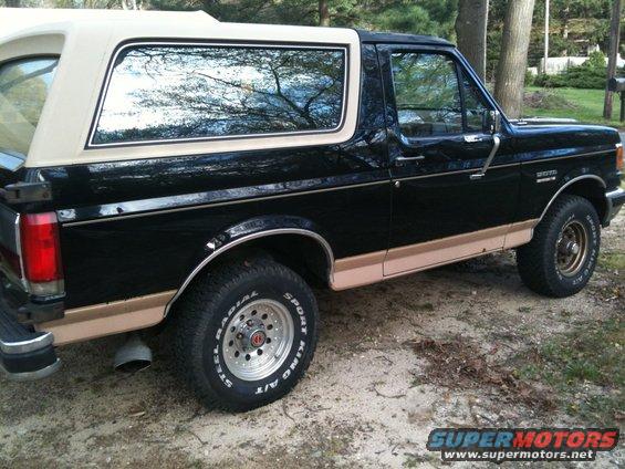 1989 Ford Bronco, black with tan trim, side view. Shows "BRONCO" badge on fender