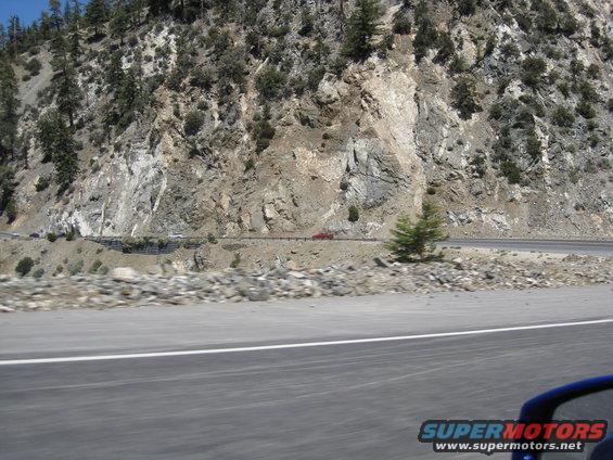 Red car driving on a winding mountain road next to a rocky cliff