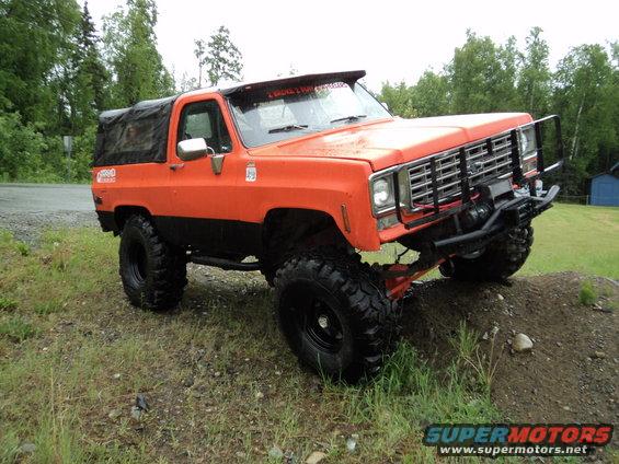 Orange off-road SUV with a soft top, lifted suspension, and large tires, angled on a dirt mound