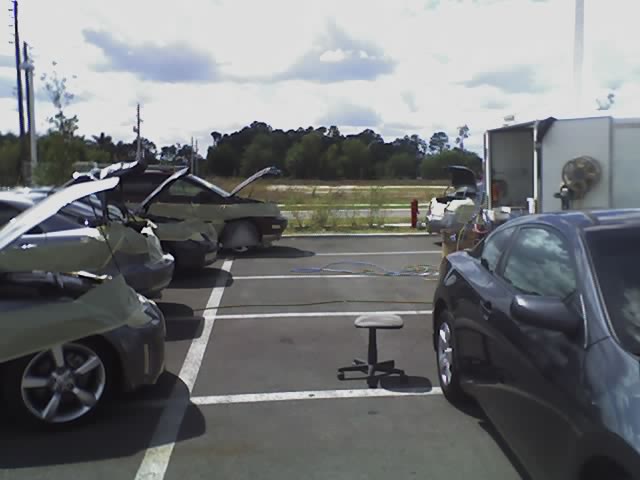 Several cars with hoods open in a parking lot, some covered with tarps