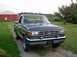 1987 Ford Bronco - This dark blue pickup truck, likely a 1987 model based on its grille, is parked on a dirt path in front of a red barn.