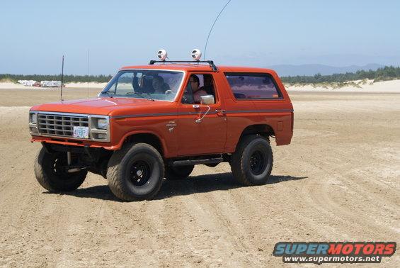 Orange Ford Bronco with roof rack and off-road tires driving on sand
