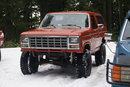Red 1980s Ford Bronco with lifted suspension and large tires, parked in snow