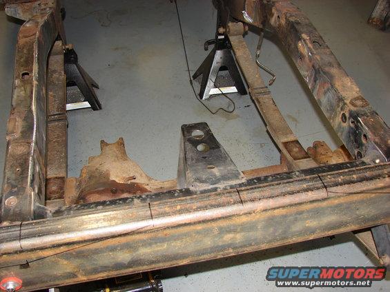 rusted vehicle frame supported by jack stands, showing leaf springs and suspension components
