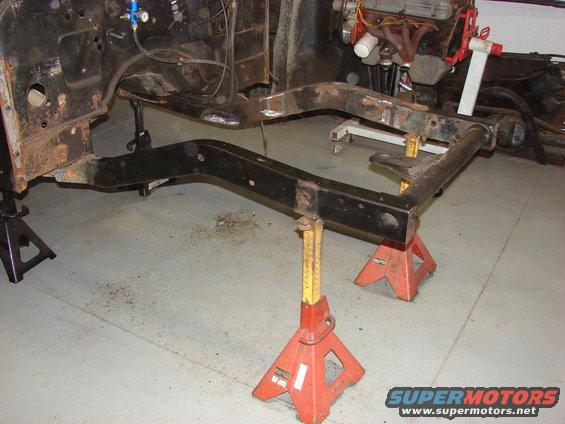 Vehicle frame and engine components on jack stands in a garage