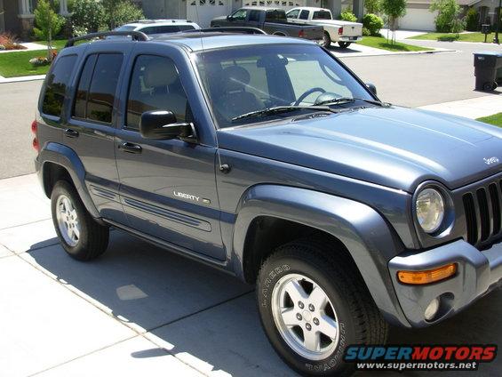 Dark blue 2002 Jeep Liberty parked in driveway with two pickup trucks behind it