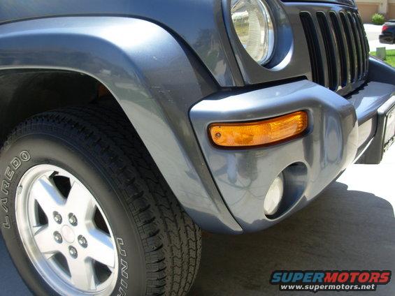 Front corner of a dark gray 2002 Jeep Liberty showing the headlight, grille, turn signal, and tire