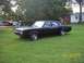 1966 Oldsmobile Cutlass - A matte black 1966 Oldsmobile Cutlass sedan sits in a grassy yard with houses in the background.