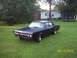1966 Oldsmobile Cutlass - A matte black 1966 Oldsmobile Cutlass sedan sits on a lawn with a house and trampoline in the background.