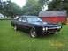 1966 Oldsmobile Cutlass - A matte black 1966 Oldsmobile Cutlass sedan is parked on a grassy lawn in front of a red barn.