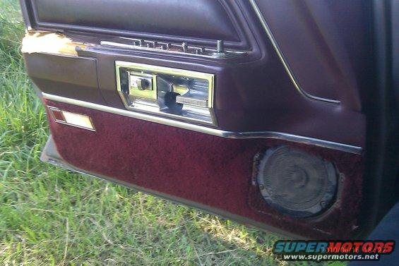 Close-up of a car's interior door panel showing the armrest, window crank, and speaker grille