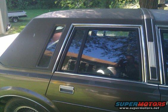 Dark sedan's rear passenger side window and vinyl roof section. Chrome trim surrounds the window