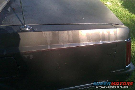 Rear quarter panel and trunk lid of a dark-colored car with a visible antenna and some paint damage