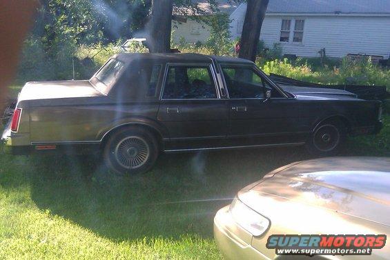 Side view of a dark 1990s Lincoln Town Car with a vinyl roof