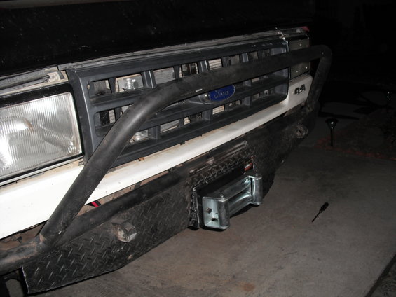 Front bumper with winch on a 1987 Ford Bronco, showing a black grille and diamond plate bumper