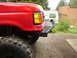 1989 Ford Bronco - A red pickup truck is shown from the front corner, a custom black bumper and large off-road tires.