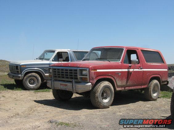 Red 1981 Ford Bronco parked next to a silver one on a dirt road