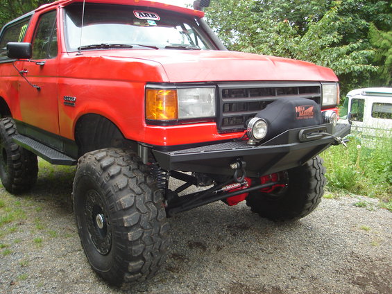 Red 1989 Ford Bronco with large tires and custom bumper