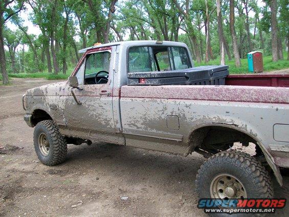 Mud-covered silver Ford pickup truck, side view, with a red bed liner and a black toolbox