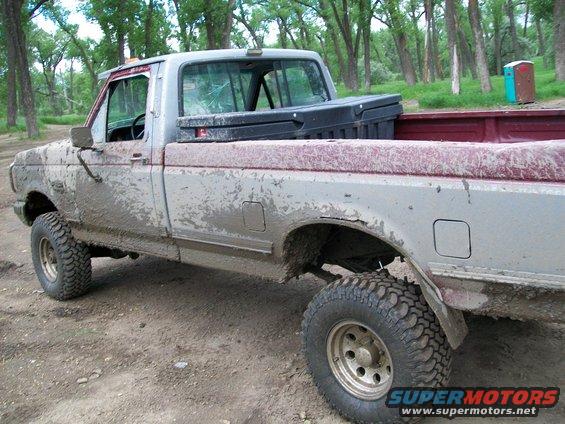 Mud-covered pickup truck parked on a dirt road with trees in the background