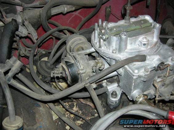 Close-up of a carburetor and engine hoses, red engine bay visible