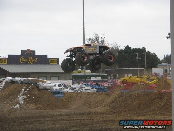 Monster truck airborne over crushed cars, with a saloon building in the background
