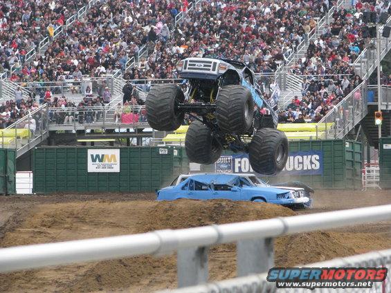 Monster truck airborne over a crushed blue sedan at a demolition derby