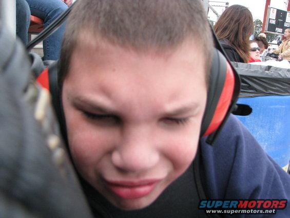 Kid with earmuffs looking upset, people in background, scoreboard visible