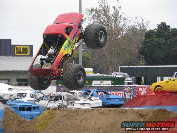 Monster truck in mid-air over crushed cars, with a saloon building in the background