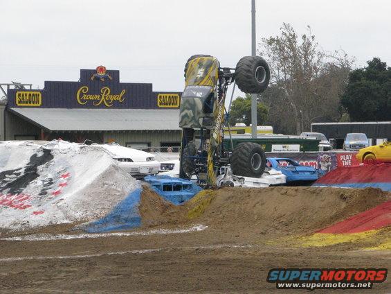 Monster truck upside down on dirt ramp, crushing cars. Crown Royal Saloon sign in background