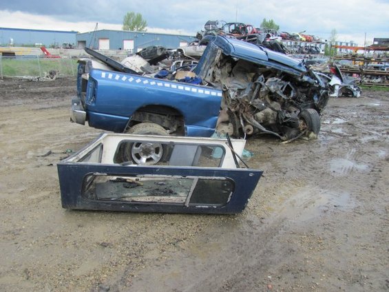 Wrecked blue 2005 Dodge 3500 pickup truck with its topper removed, piled with other scrap vehicles