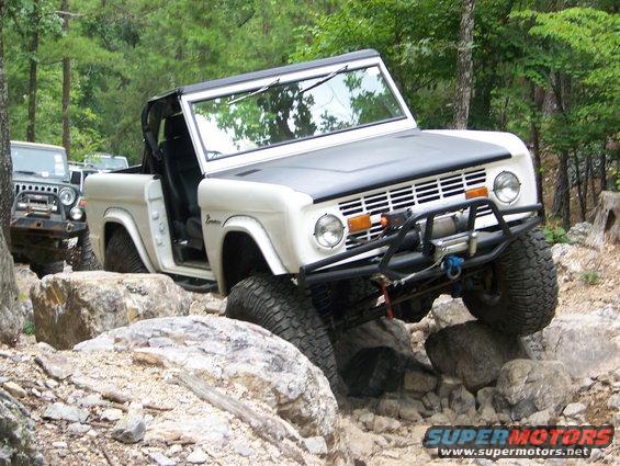White Ford Bronco climbing over rocks on a trail, with a Jeep behind it