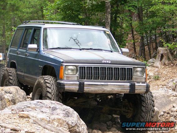 Blue Jeep Cherokee XJ with large tires crawling over rocks