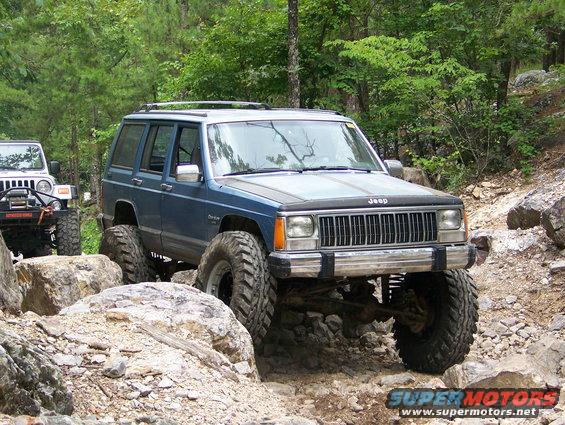 Blue Jeep Cherokee with lifted suspension and large tires on a rocky trail
