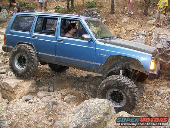 Blue Jeep Cherokee XJ with large off-road tires navigating rocky terrain