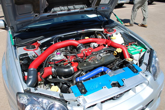 Engine bay of a silver 2005 Subaru Impreza with red intake piping and blue intercooler piping
