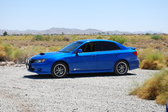 Blue sedan parked on gravel with desert landscape behind it