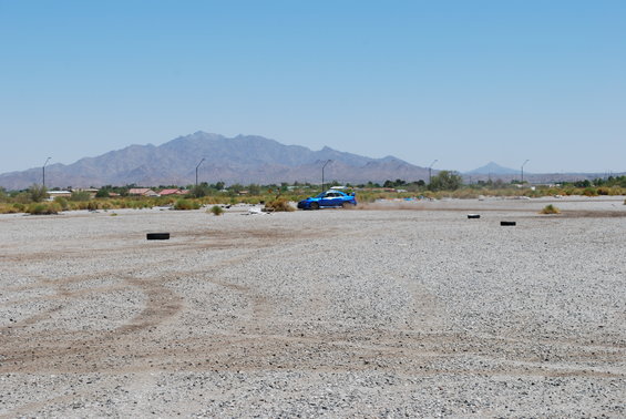 Blue Subaru WRX driving on a gravel lot with mountains in the background