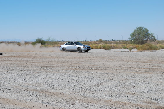 Silver 2005 Subaru Impreza drifting on a gravel lot, kicking up dust