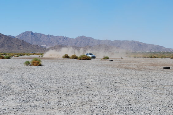 Silver SUV driving on a dusty, gravelly plain with mountains in the background