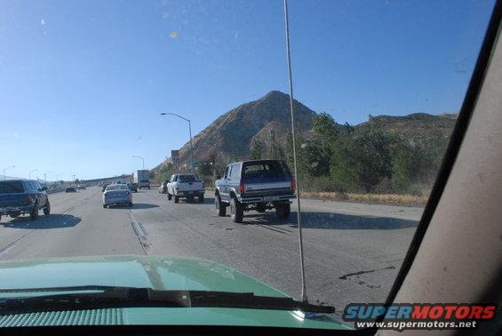 Blue Ford Bronco driving on highway, rear view. Lifted suspension, aftermarket wheels