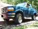 1995 Ford Bronco - This blue Ford Bronco is parked on a gravel driveway with trees in the background.