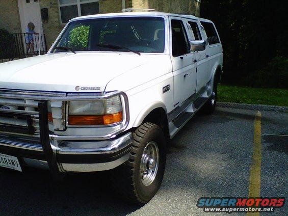 White extended cab pickup truck with a camper shell parked in a lot. It has a chrome grille guard and running boards
